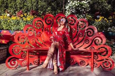 Portrait young woman sitting on bench against plants