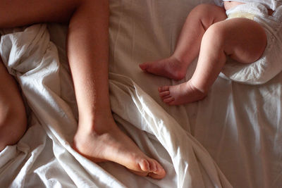 Upper view on feet of elder child and newborn baby on the bed