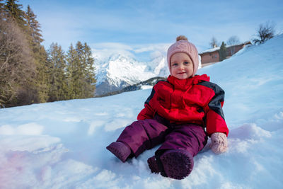 Portrait of boy sitting on snow covered field against sky
