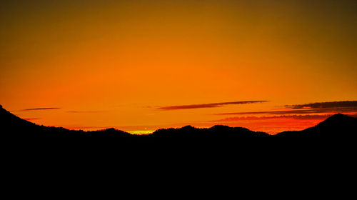 Scenic view of silhouette mountains against orange sky