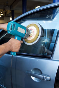 Cropped hands of man polishing car window in auto repair shop