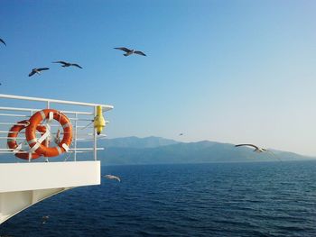 Seagulls flying by ship in sea against clear sky