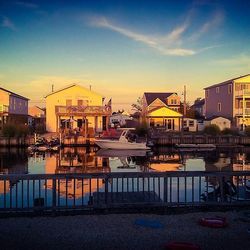 Buildings by lake against sky at sunset