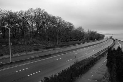 Empty road by trees against sky in city