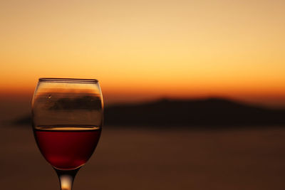 Close-up of wineglass against orange sky during sunset