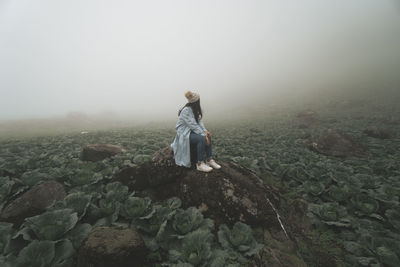 Full length of woman sitting on rock in farm