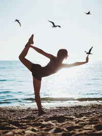 Woman doing yoga at beach against sky