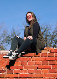 Portrait of smiling young woman sitting against brick wall