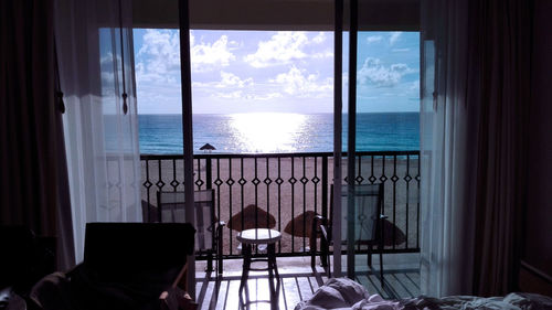 Chairs and table by sea against sky seen through window