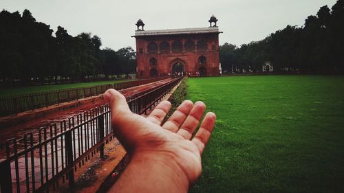 Cropped image of hand by built structure against sky