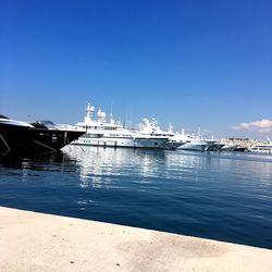 Boats moored at harbor against clear blue sky