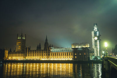 Illuminated buildings by river against sky in city at night