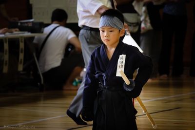 Boy in kendo uniform looking down while standing on floor