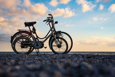 Bicycle parked on rock against sky during sunset