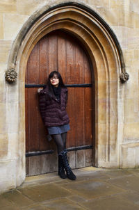 Portrait of smiling young woman standing against door