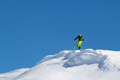 Man skiing on snowcapped mountain against clear blue sky