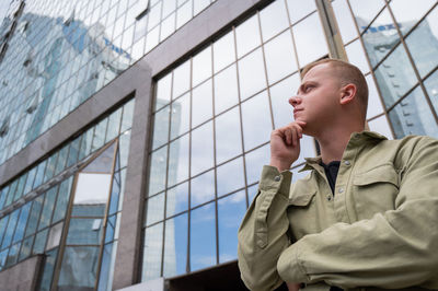 A pensive man stands against the backdrop of a skyscraper