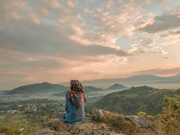 Rear view of woman standing on mountain against sky during sunset