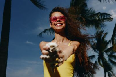 Low angle view of young woman looking away while standing against sky