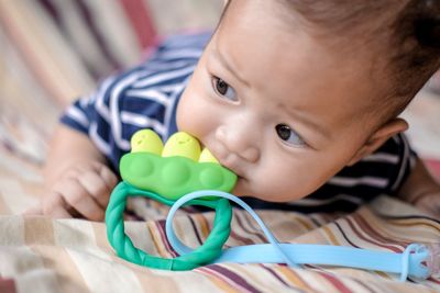 Close-up of cute baby boy playing with toy while lying on bed at home