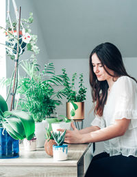 Young woman with potted plants on table at home