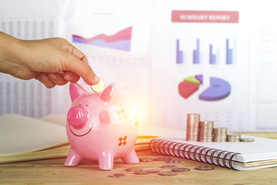 Close-up of business person inserting coin in piggy bank at office