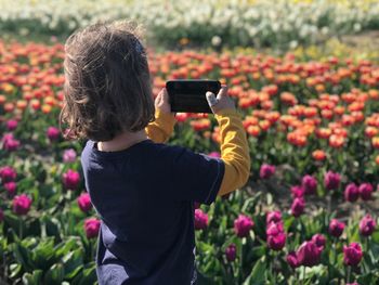 Rear view of boy photographing on mobile phone by plants