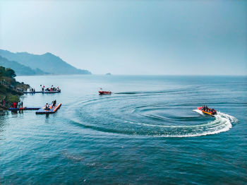 People on boats in sea against clear sky