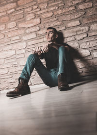 Full length of man sitting against wall
