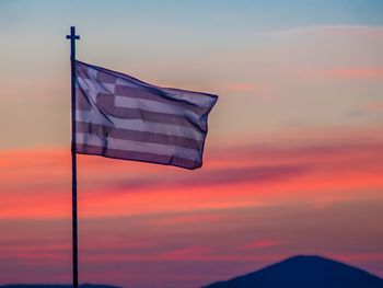 Low angle view of flag waving against dramatic sky during sunset