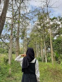 Rear view of woman standing amidst trees in forest