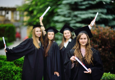 Portrait of smiling woman holding diploma standing in front of friends