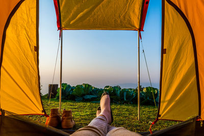 Low section of woman in tent on field against sky during sunset