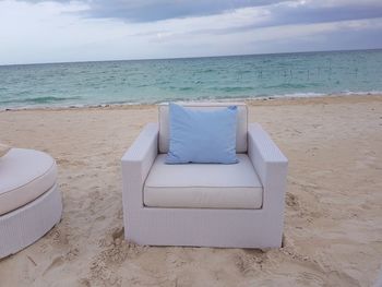 Deck chairs on beach against sky