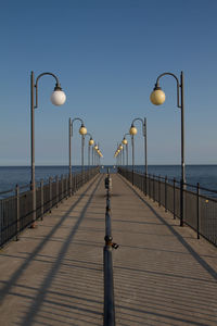 Street lights on pier by sea against clear sky