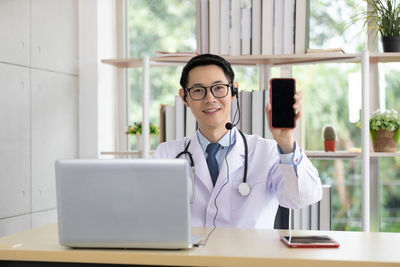 Portrait of smiling doctor showing mobile phone while sitting at hospital