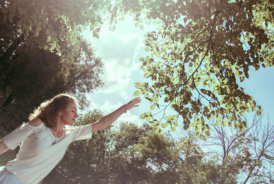 Teenage girl reaching towards tree against sky