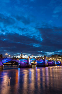 Illuminated bridge over river against cloudy sky