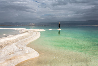 Rear view of woman practicing at dead sea against cloudy sky