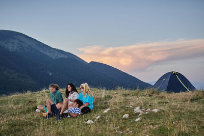 Group of people sitting on mountain against sky