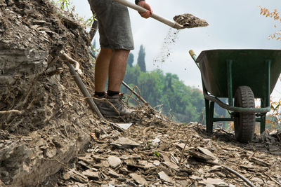 Low section of man collecting dirt in wheel barrow