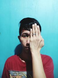 Portrait of young man covering face against blue wall