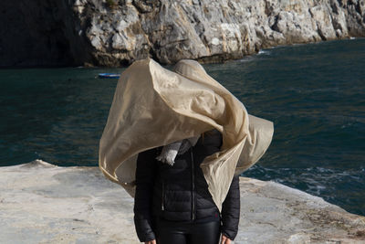 Rear view of woman standing on rock by sea