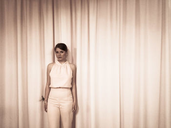 Young woman standing against curtain