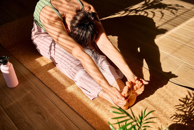 Woman practicing yoga and meditation at home sitting on yoga mat, stretching muscles of legs. 