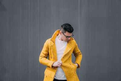Young man wearing yellow jacket against gray wall