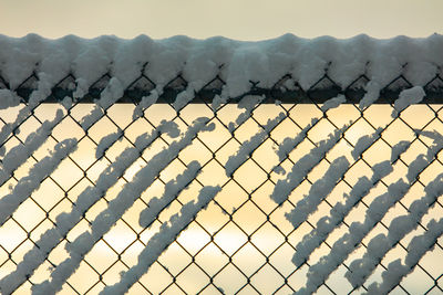 Fence on snow covered landscape against sky