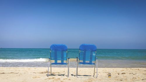 Two beach chairs facing sea against clear blue sky