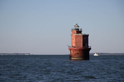 Lighthouse by sea against clear sky