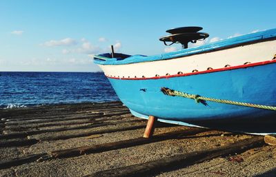 Boat moored on beach against blue sky